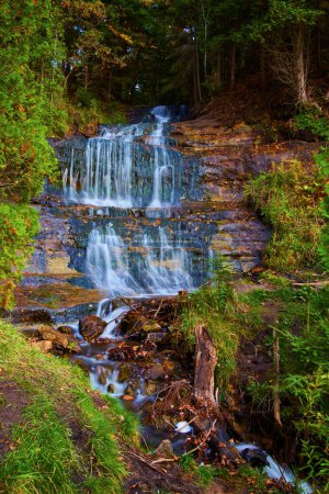Serene Autumn Waterfall at Alger Falls, Michigan - A scenic capture of the peaceful cascading water flow over rock ledges, surrounded by the changing colors of the dense forest.