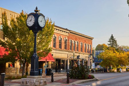 Photo for Historic Plymouth clock in serene small-town Michigan, lined by quaint brick storefronts and lush autumnal trees during golden hour - Royalty Free Image