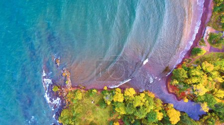 Aerial view of serene Copper Harbor, Michigan in fall displaying vibrant foliage meeting azure Lake Superior waters