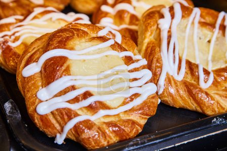 Freshly baked Danish pastries with creamy custard filling and white icing on a dark tray, Bakery in Fort Wayne, Indiana, 2017