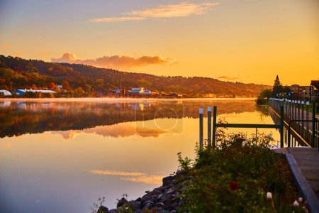Serene autumn sunrise over a tranquil lake in Houghton, Michigan, reflecting a quaint town nestled among the trees, 2017