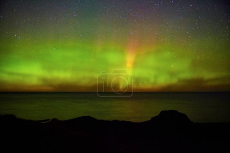 Foto de Impresionante Aurora Boreal sobre un océano sereno y un terreno rocoso en Copper Harbor, Michigan, creando un fascinante espectáculo de cielo nocturno en 2017. - Imagen libre de derechos