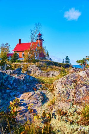 Tagsüber Blick auf den historischen Eagle Harbor Leuchtturm auf einer felsigen Klippe am Lake Superior, Michigan, umgeben von Herbstlaub und einem klaren blauen Himmel.