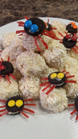 Playful dessert presentation with coconut-covered treats and whimsically decorated cookie spiders on a simple white plate, evoking a festive and creative mood