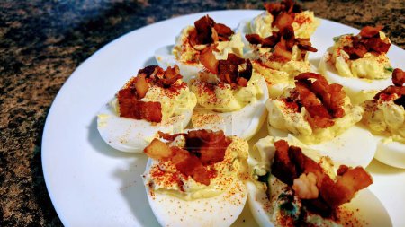 Delicious homemade deviled eggs garnished with paprika and bacon, served on a white plate in a cozy domestic kitchen in Fort Wayne, Indiana, 2021 - a classic taste of Midwest home cooking.