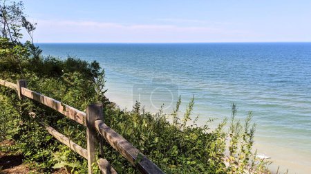 Sunny Coastal Day at Casco Nature Preserve Michigan, Featuring Calm Turquoise Waters, Lush Greenery, and Quaint Wooden Fence