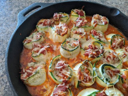 Freshly baked zucchini rolls with melted cheese and tomato sauce in a cast iron skillet, symbolizing home cooking and healthy eating