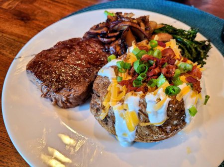 Gegrilltes Steak mit beladenen Ofenkartoffeln und sautiertem Gemüse auf einem Holztisch, perfekt zur Feier von Hausmannskost und Geburtstagen in Fort Wayne, Indiana, 2022.