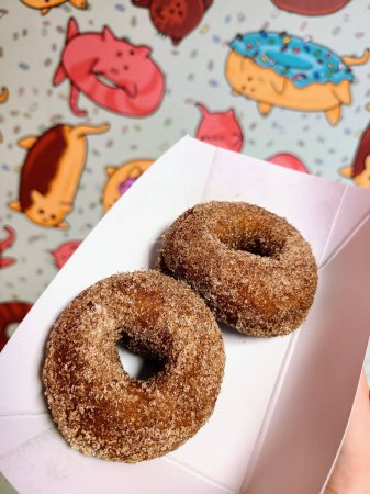 Foto de Donuts recién horneados y azucarados en una caja blanca, contra un fondo de pantalla juguetón y colorido con dibujos de gato, en un restaurante de Auburn, Indiana, 2023. - Imagen libre de derechos