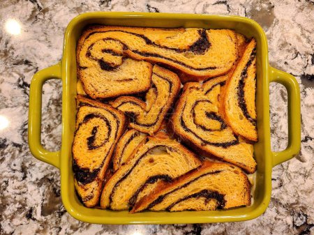 Freshly baked artisanal cinnamon roll bread pudding in a vibrant yellow dish on a marble countertop, symbolizing home cooking and festive warmth, Fort Wayne, Indiana, 2021