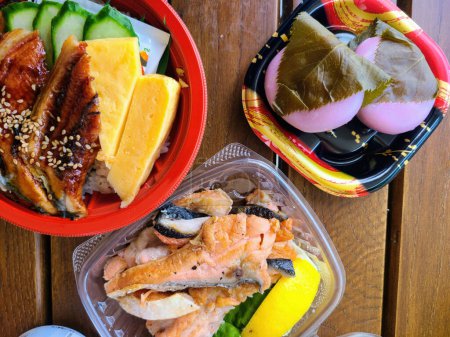 Cajas de bento japonesas frescas con salmón a la parrilla, anguila y onigiri en una mesa de madera rústica en Columbus, Ohio, 2023, que simboliza la dieta equilibrada y la cocina tradicional.