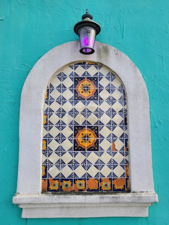 Lebendige traditionelle Laterne beleuchtet verzierte Fliesennische im spanischen Stil an kühner türkisfarbener Wand und weckt historischen Charme in Mount Vernon, Ohio
