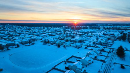 Aerial view of a peaceful, snow-clad suburban neighborhood in Fort Wayne, Indiana, basking in the warm glow of an early winter sunrise.