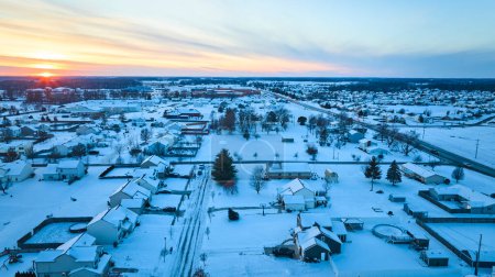Winter sunset blankets a tranquil Fort Wayne suburban neighborhood in snow, offering an idyllic aerial view of residential life.