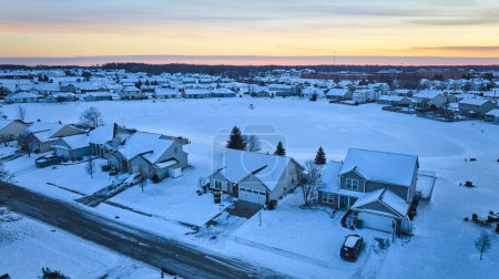 Vista aérea de un tranquilo suburbio de invierno en Fort Wayne, Indiana, al anochecer con casas cubiertas de nieve y calles