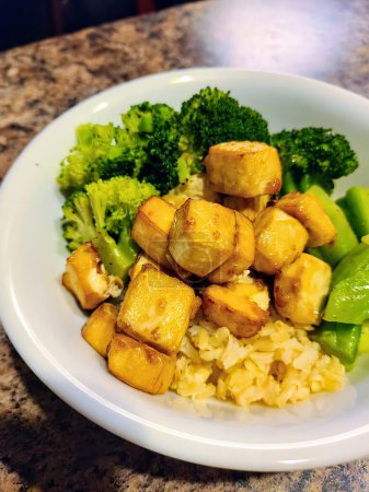 Einladende vegane Mahlzeit mit knusprigem Tofu, frischem Brokkoli und würzigem gelben Reis, zubereitet und serviert in einer heimeligen indianischen Küche.