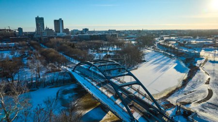 Winter afternoon paints a serene cityscape of downtown Fort Wayne, Indiana, with the sleek Martin Luther King Bridge arching over the frozen St. Marys River.
