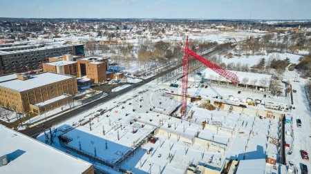 Winterliche Stille über einer Baustelle in der Innenstadt von Fort Wayne, Indiana, als ein roter Kran die schneebedeckte Stadtlandschaft durchschneidet.