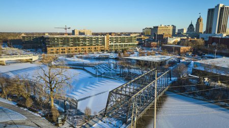 Lever de soleil hivernal au-dessus de Fort Wayne, Indiana, mettant en valeur le pont neigeux de Wells Street, la rivière St. Marys et l'évolution des toits de la ville.