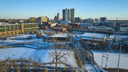 Wintermorgen in Fort Wayne, Indiana, eine Luftaufnahme fängt den schneebedeckten Promenade Park und den St. Marys River ein, der die Skyline der Stadt umrahmt.