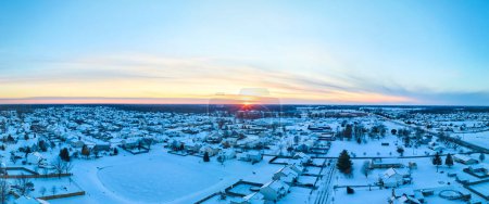 Luftaufnahme eines schneebedeckten Vorortviertels in Fort Wayne, Indiana, im warmen Schein eines winterlichen Sonnenuntergangs.