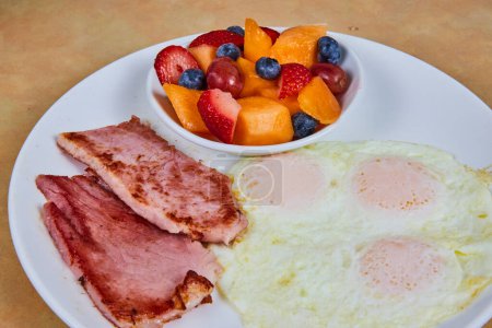Klassischer amerikanischer Frühstücksaufstrich in Fort Wayne, Indiana, mit sonnenbeschienenen Eiern, gegrilltem Schinken und einem lebhaften Fruchtmix.