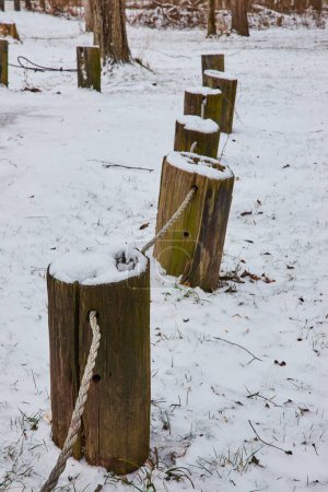 Früher Schneefall drapiert verwitterte Holzpfähle und Seile im ruhigen Cooks Landing County Park, Indiana und malt eine ruhige Winterlandschaft.