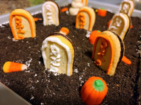 Spooky Delight: Close-up of Halloween-inspired dessert graveyard, made of iced cookie tombstones and candy pumpkins on a cookie crumb soil - a festive treat from Indiana.