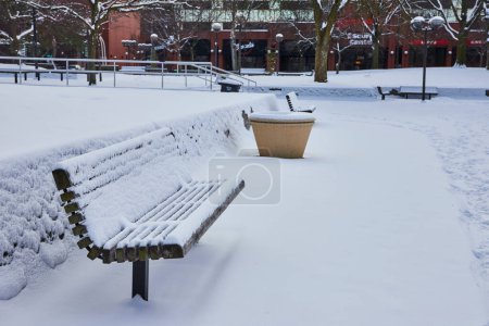Paisajista escena invernal en Fort Waynes Freimann Square, mostrando bancos cargados de nieve y una huella solitaria.