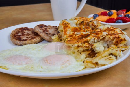Ein einladendes amerikanisches Frühstück in Fort Wayne, Indiana, mit sonnenbeschienenen Eiern, Würstchen, Hasch-Bräunen und frischem Obst - ein perfekter Start in einen lebhaften Morgen.