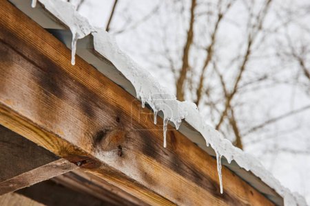 Schmelzende Eiszapfen hängen an einer rustikalen Holztraufe und fangen das ruhige Tauwetter des Winters im Cooks Landing County Park, Indiana, ein..