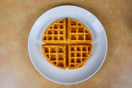 Overhead view of a golden breakfast waffle cut into pieces, ready to enjoy on a minimalistic beige background, Fort Wayne, Indiana