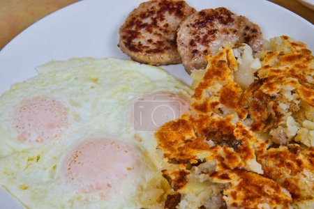 Desayuno americano abundante con huevos soleados, papas fritas crujientes y salchichas saladas, evocando comodidad hogareña en Fort Wayne, Indiana.