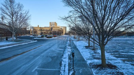 Winter sunrise paints a peaceful scene in downtown Fort Wayne, Indiana, featuring a snow-laden street, bare trees, and iconic architecture.