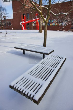 Peaceful winter scene in Fort Wayne, Indiana with fresh snow blanket on park bench, barren tree and vibrant public art