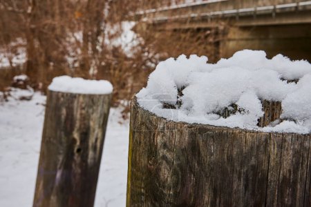 Ruhige Winterszene im Cooks Landing Park, Indiana, mit Neuschnee auf rustikalen Holzpfählen und einer entfernten Brücke