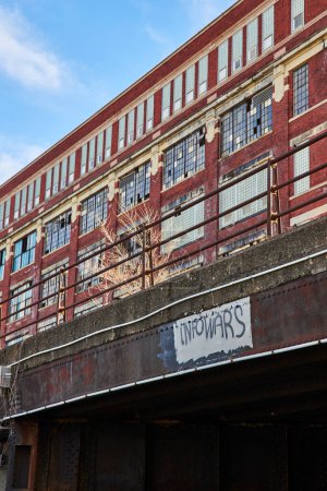Téléchargez les photos : La décadence urbaine rencontre l'histoire à Fort Wayne - Passerelle graffifiée et édifice industriel abandonné sous un ciel bleu clair - en image libre de droit