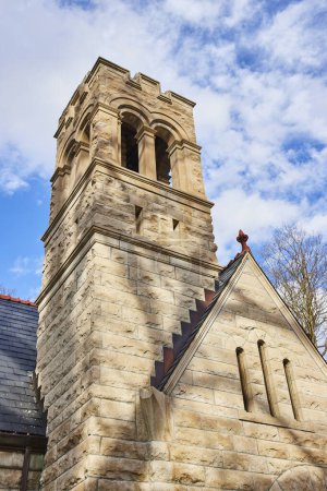 Imposing stone tower from historic church, displaying craftsmanship and durability, rising against a partly cloudy sky in Lindenwood Cemetery, Fort Wayne, Indiana.