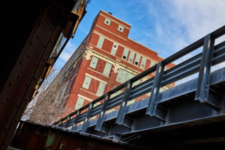 Un bâtiment classique en brique rouge et un pont industriel robuste révèlent la riche histoire architecturale de Fort Waynes sous un ciel dégagé.