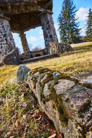 Moosbewachsene Steine führen zu historischen Ruinen unter sonnigem Himmel auf dem Lindenwood Cemetery, Fort Wayne, und fangen die Urbarmachung der Architektur durch die Natur ein.