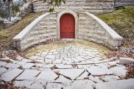 Enchanting red door in stone structure at Lindenwood Cemetery, Indiana, exuding a sense of mystery and tranquility amidst autumnal setting.