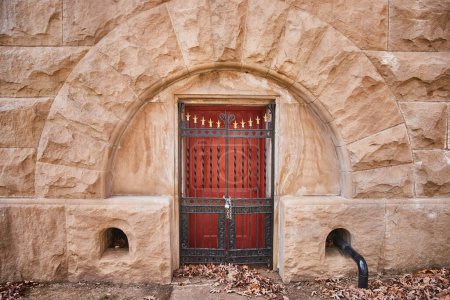 Antique red door with ironwork in a stone archway at Lindenwood Cemetery, Indiana, symbolizing history, mystery, and autumns passage.