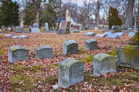 Time-stamped headstones and historic chapel amidst barren trees at Lindenwood Cemetery, Fort Wayne, Indiana in autumn.