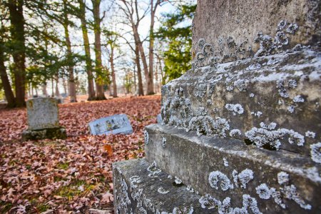 Automne au cimetière Lindenwood, Indiana - Nature morte paisible d'une pierre tombale altérée parmi les feuilles tombées.