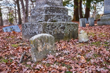 Peaceful autumn scene at Lindenwood Cemetery in Fort Wayne, Indiana showcasing moss-covered gravestones amidst a carpet of fallen leaves.