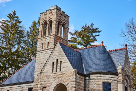 Romanesque Revival stone chapel with robust bell tower in Lindenwood Cemetery, Fort Wayne, Indiana, under clear blue sky.