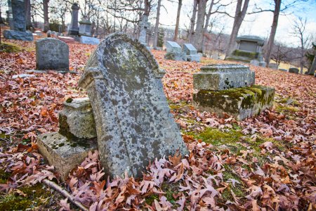 Tranquilidad a finales del otoño en el cementerio de Lindenwood, Fort Wayne, Indiana, revelando la belleza duradera de lápidas erosionadas en medio de hojas caídas.