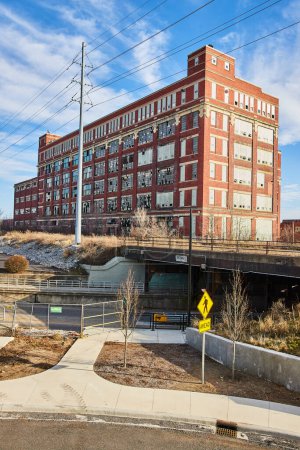 Fábrica de ladrillos vintage en Electric Works, Fort Wayne, bajo cielos despejados, fusionada con un paisaje urbano moderno que muestra la renovación urbana.