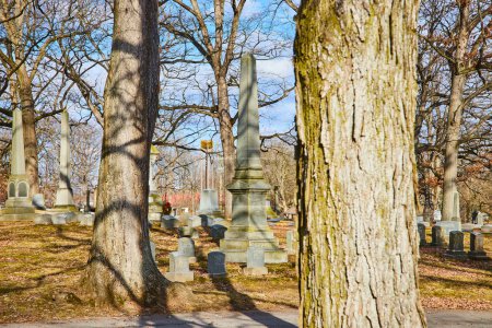 Peaceful autumn afternoon at Lindenwood Cemetery, Fort Wayne, Indiana, featuring a historic obelisk amidst bare trees and aged gravestones.