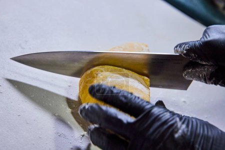 Hands in black gloves slice through raw dough wedge with a high-quality chefs knife, showcasing the art of food preparation in a professional kitchen in Fort Wayne, Indiana. Perfect for culinary
